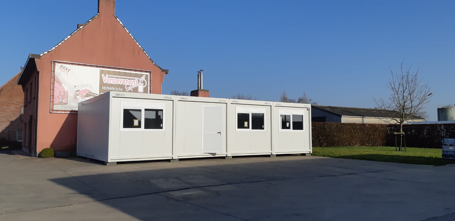 Gekoppelte modulare Büroeinheiten mit großen Fenstern und Rollläden an einer Tankstelle
